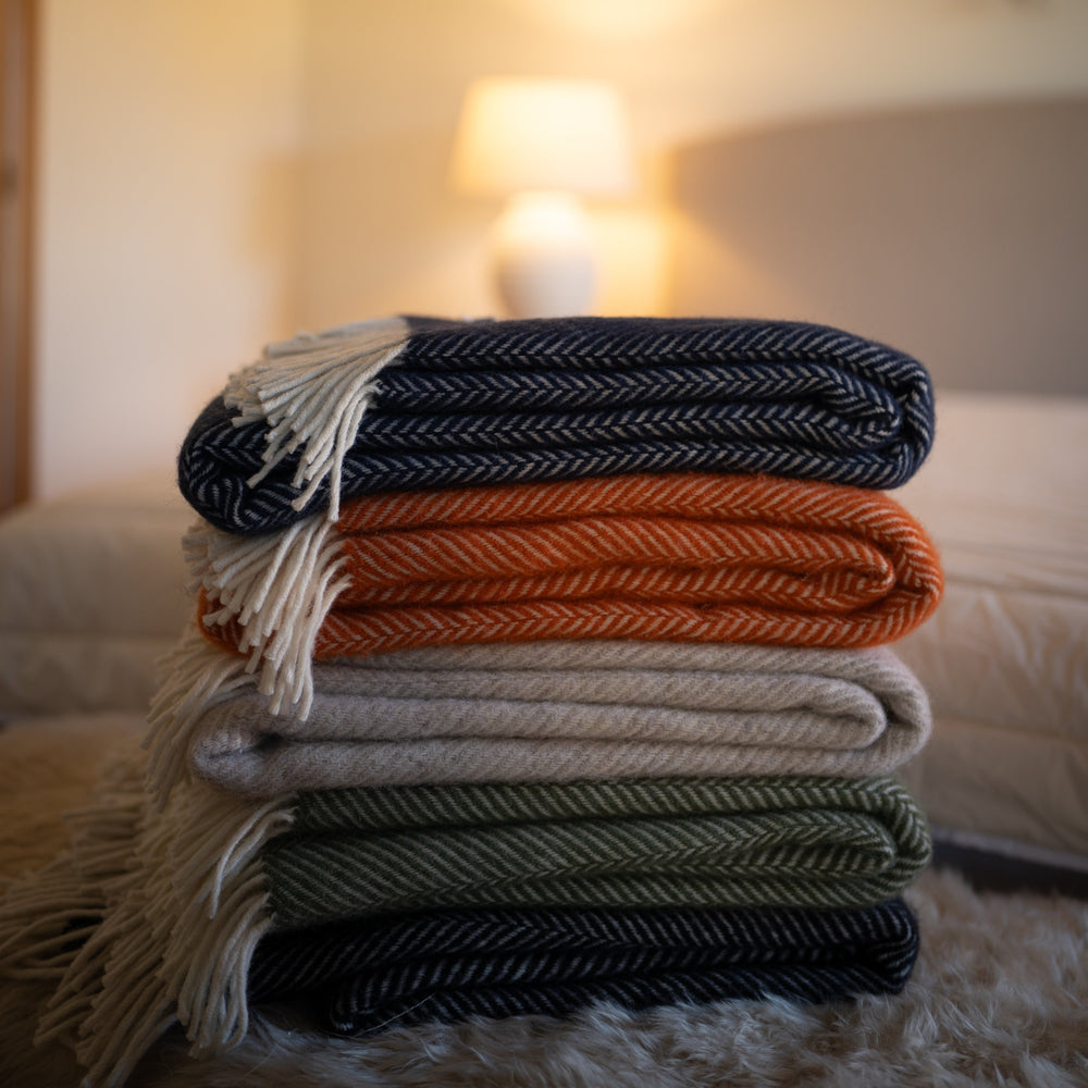 Floks wool throws in various colours stacked on a bed in a bedroom