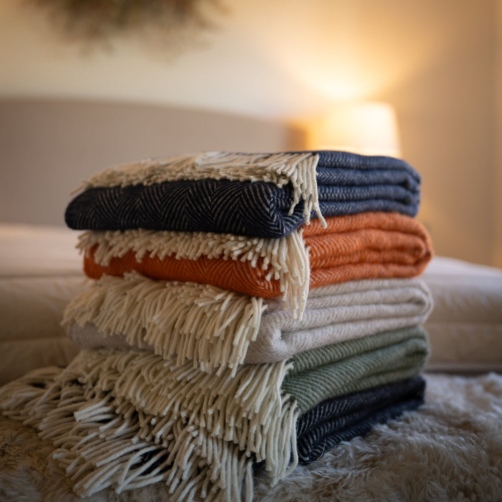 Floks wool throws in various colours stacked on a bed in a bedroom