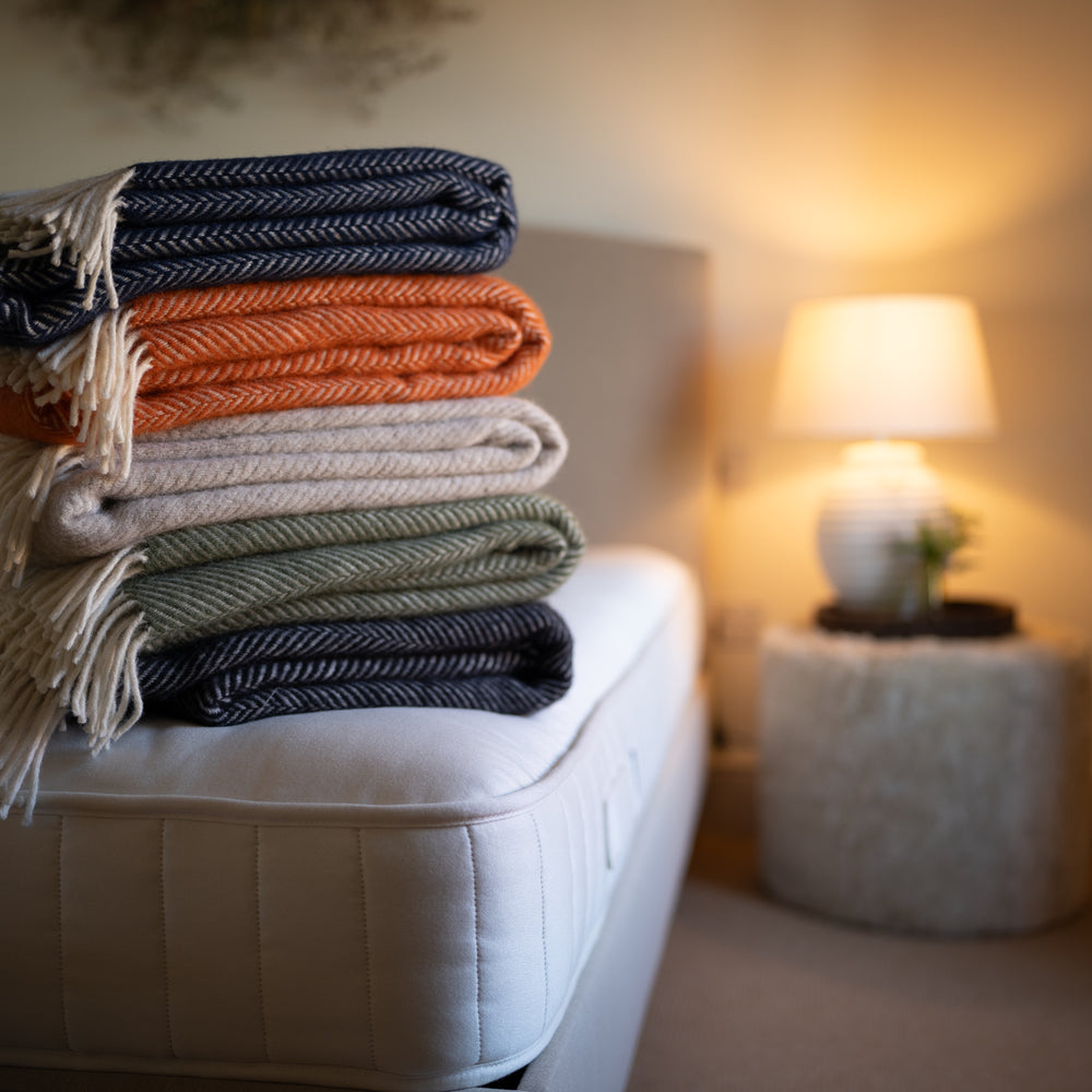 Floks wool throws in various colours stacked on a bed in a bedroom