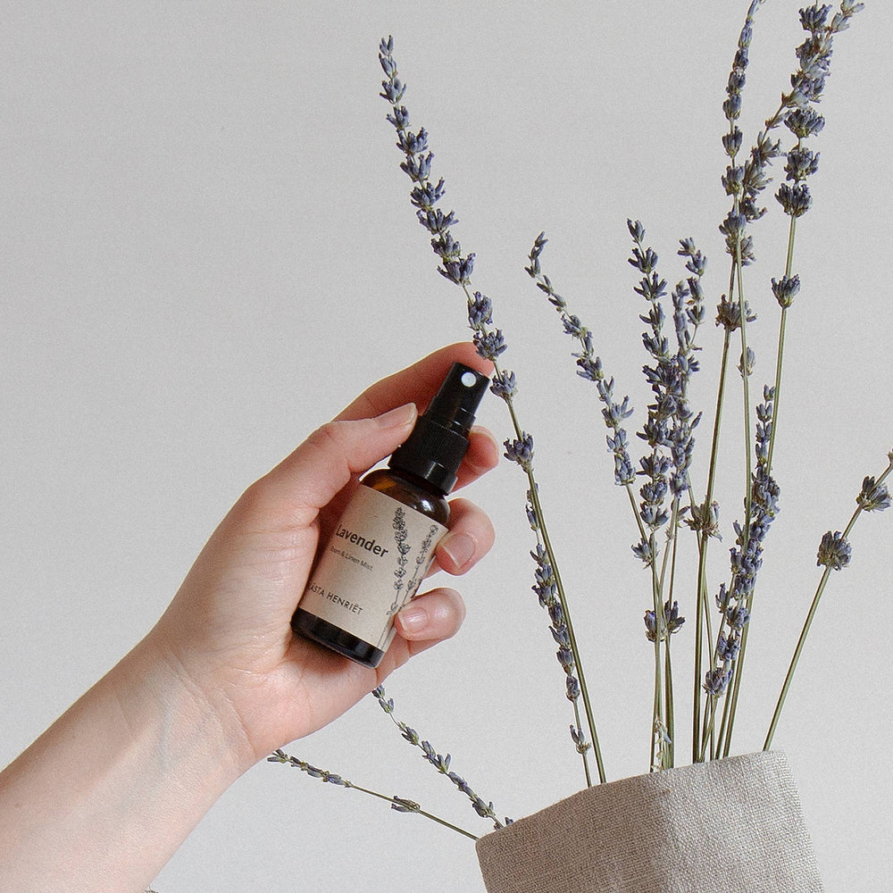 Blästa Henriët Room + Linen Mist with a hand holding the bottle and lavender alongside 