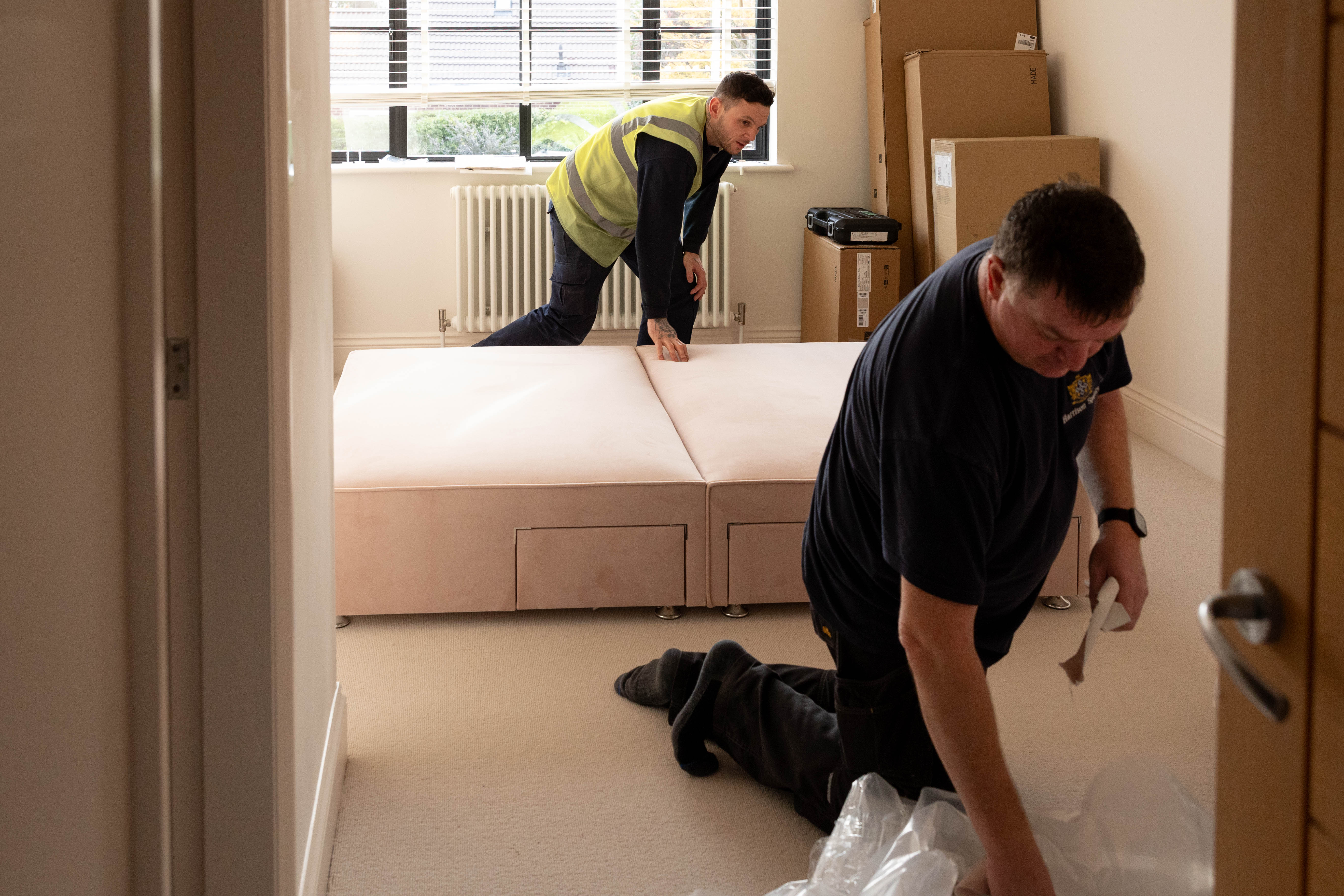 Two men working on assembling a sectional sofa in a room with a radiator and window.