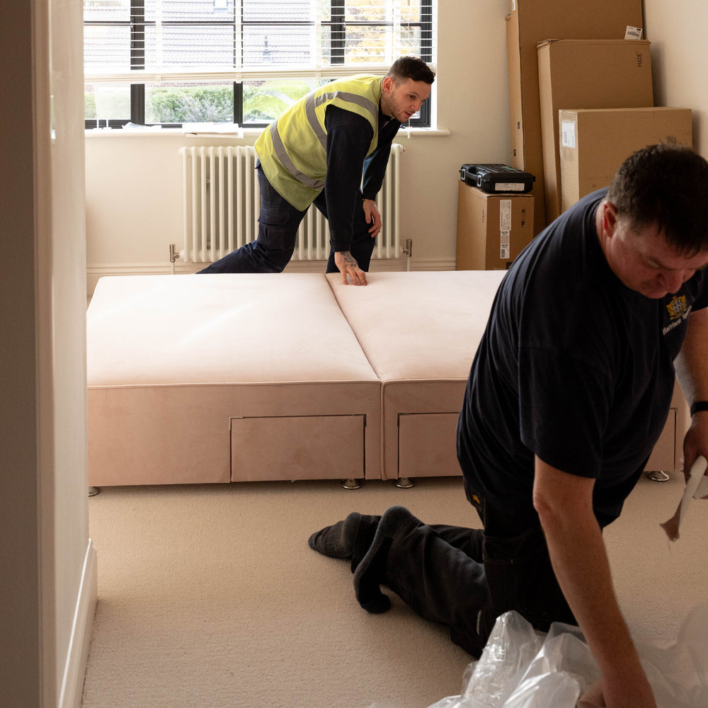 Two men working on assembling a sectional sofa in a room with a radiator and window.